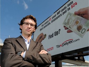 Scott Hennig, of the Canadian Taxpayers Federation stands in front of a billboard his organization put up in downtown Calgary, Alberta in 2012 bringing attention to the lavish pension plans for MPs. File photo.