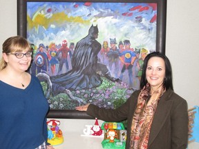 Kids Kottage marketing and communications director Melissa Barr, left, and executive director Janine Fraser join a gathering of imaginary superheroes. The painting is the work of Lewis Lavoi and was sold at a Kids Kottage fundraiser and donated to the shelter by the buyer.