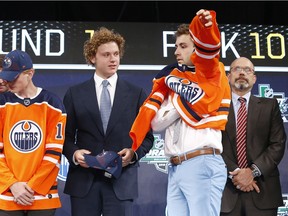 Evan Bouchard, second from right, of Canada, puts on a jersey after being selected by the Edmonton Oilers during the NHL hockey draft in Dallas, Friday, June 22, 2018.