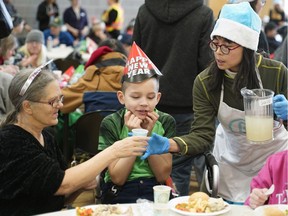 Volunteer Karen Louie (right) serves a beverage to Barb Johnson (left) and Andrew Hutchinson (middle) at the Bissell Centre's New Year's Day dinner held at Boyle Street Plaza on Jan. 1, 2019.