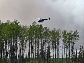 A helicopter flys tree-top level ahead of wildfire crews doing controlled burn ignition operation on May 23, 2019, approximately three kilometres southwest of High Level where about 4,000 residents were evacuated from the Chuckegg Creek fire.