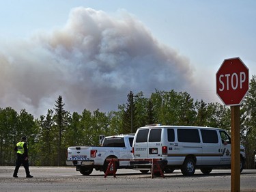 Police are seen at the north end of High Level's road blockade as wildfire crews doing controlled burn ignition operation approximately three kilometres southwest of the town on Thursday, May 23, 2019.