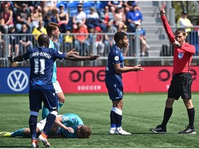 An official gives a red card to FC Edmonton's Philippe Lincourt- Joseph (centre) for tripping up Pacific FC Ryan McCurdy (3) during their Canadian Premier League home opener at Clarke Stadium in Edmonton on May 12, 2019.