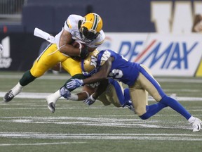 Calvin McCarty (31) gets hit by Winnipeg Blue Bombers' Anthony Gaitor (23), and another Bomber during CFL action in Winnipeg today. Thursday, June 14, 2018.