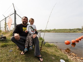 Blair Brazeau fishes while his son Hunter, 4, plays in the river as a wildfire evacuation alert continues in the town of Slave Lake, on Saturday, June 1, 2019.