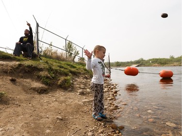 Blair Brazeau fishes while his son Hunter, 4, plays in the river as a wildfire evacuation alert continues in the town of Slave Lake, on Saturday, June 1, 2019.