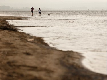 A couple walk along Devonshire Beach as a storm rolls during a wildfire evacuation alert continues in the town of Slave Lake, on Saturday, June 1, 2019.