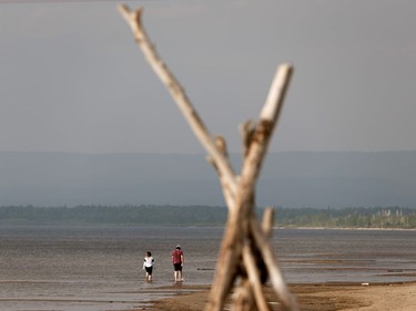 A couple walk along Devonshire Beach as a storm rolls during a wildfire evacuation alert continues in the town of Slave Lake, on Saturday, June 1, 2019.