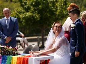 Marni Panas, seated, and Kate Beneteau sign their wedding papers during their marriage at Patricia Lake Park in Edmonton, on Sunday, June 30, 2019.