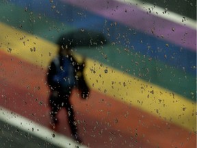 A pedestrian makes their way through the rain near 109 Street and 104 Avenue, in Edmonton Thursday June 20, 2019. The crosswalk had been painted for Pride Month.