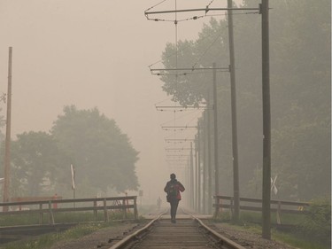 A pedestrian walks through the smoke along the High Level Bridge Streetcar line, near 105 street and 85 Avenue, in Edmonton Thursday May 30, 2019. Smoke from northern wild fires has blanketed the Edmonton region. Photo by David Bloom