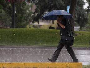 A man walks along MacDonald Drive near 102 Street in the pouring rain during a thunderstorm reading his phone in Edmonton, on Wednesday, July 17, 2019.
