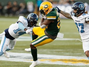 Edmonton Eskimos' Shaquille Cooper (25) is tackled by Toronto Argonauts' Adbul Kanneh (14) and Anthony Covington (37) during the first half of a CFL football game at Commonwealth Stadium in Edmonton, on Thursday, July 25, 2019.