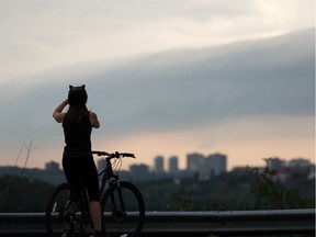 A cyclist wearing a cat eared helmet takes photos as a thunderstorm hits the city in Edmonton, on Friday, Aug. 2, 2019.