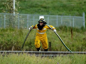 A firefighter carries a hose over a railway track while battling a grass fire near 17 Street and Whitemud Drive Monday afternoon August 26, 2019.