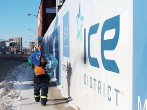 An unidentified man carrying bags of clothing in subzero temperatures walks by a barrier wall advertising the Ice District.