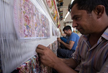 A rugmaker hand tying a new rug, using the artist's design as a reference.
