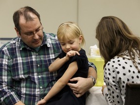 Dr. Chris Sikora, medical officer of health for Edmonton, helps his daughter Ella get her influenza vaccination from registered nurse Shantel Trenholm during a press conference at East Edmonton Health Centre in Edmonton, Alberta on Monday, October 23, 2017.