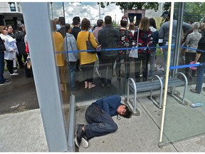 A man sleeps in a bus shelter as people lay commemorative flowers (in back) at the 14th annual service to honour people, 95 for 2018, who have died in situations of homelessness or poor housing at the Homeless Memorial Plaza  across from city hall in Edmonton, June 26, 2019.