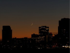 A sliver of a moon is seen behind downtown after sunset from 77 Street and Jasper Avenue during warm winter weather in Edmonton, on Friday, Dec. 27, 2019.