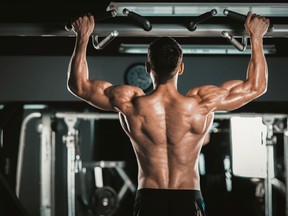 Athlete muscular fitness male model pulling up on horizontal bar in a gym.