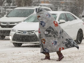 A walker uses a NHL blanket to shelter against the snow and wind as they cross 103A Avenue at 96 Street during a snowstorm in Edmonton, on Wednesday, Jan. 8, 2020.