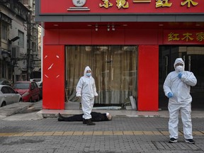 This photo taken on January 30, 2020 shows officials in protective suits checking on an elderly man wearing a facemask who collapsed and died on a street near a hospital in Wuhan. - AFP journalists saw the body on January 30, not long before an emergency vehicle arrived carrying police and medical staff in full-body protective suits.