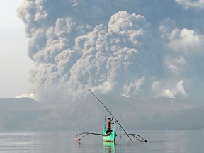 A youth living at the foot of Taal volcano poles an outrigger canoe while the volcano spews ash as seen from Tanauan town in Batangas province, south of Manila, on January 13, 2020.