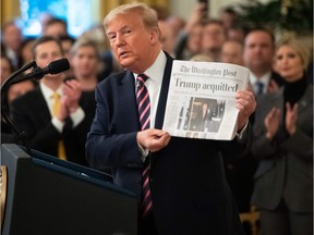 U.S. President Donald Trump holds up a newspaper that displays a headline "Acquitted"  while speaking about his Senate impeachment trial in the East Room of the White House in Washington, DC, Feb. 6, 2020.