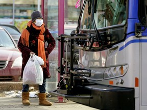 A woman, wearing a face mask for protection against COVID-19, waits to board a public bus in downtown Edmonton on March 17, 2020. There were reports of overcrowded buses Monday after the city started running public transit buses on reduced weekend scheduling because of the coronavirus pandemic.