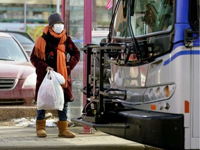 A woman wearing a face mask waits to board an Edmonton transit bus in downtown Edmonton on March 17, 2020.