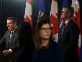 Premier Jason Kenney (left) is seen in a mirror giving an update with government ministers on COVID-19 assistance for families and businesses from the media room at the Alberta Legislature in Edmonton, on Wednesday, March 18, 2020.