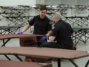 Firefighters Mitch Penner (left) and Rory Young helped set up cots at the Edmonton Expo Centre on Friday March 20, 2020, where an emergency COVID-19 isolation shelter was being set up for the city's homeless population. The isolation shelter is now being moved to another undisclosed location in the city.