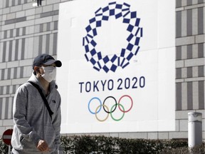 A pedestrian wearing a protective face mask walks past a banner featuring the emblem for the Tokyo 2020 Olympic Games in Tokyo, Japan, on Wednesday, March 11, 2020.