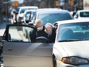 An elderly man wears a mask while helping a woman into a vehicle after leaving the hospital in Toronto on Friday, March 27, 2020. People are taking extra measures against the spread of the coronavirus also known as COVID-19.