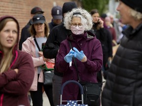 A shopper pulls on rubber gloves while standing in a long line of COVID-19 social distancing customers outside the Old Strathcona Farmers Market, in Edmonton Saturday May 23, 2020.