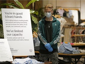 An employee in the Aritzia clothing store at Southgate Centre shopping mall in Edmonton takes precautions during the COVID-19 pandemic on Thursday May 14, 2020, when the Alberta government allowed retail stores to re-open for business.