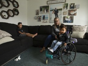 Lana Bernardin helps her son Kaysen Martin, 1, into the family living room, in Edmonton Thursday July 2, 2020. Her oldest son Blake Martin, 4, is also pictured (left).  Kaysen has a rare motor neuron disease called Spinal Muscular Atrophy Type 1 (SMA 1). His family has met all approvals to get a new drug called Zolgensma administered to help keep Martin alive and healthy, but it costs $2.8 million and isn't covered in Alberta.