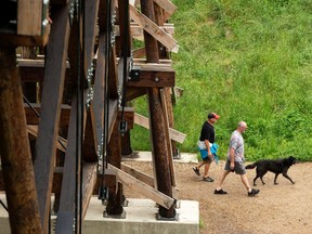 Dog walkers are seen on a trail under a walking bridge in Mill Creek Ravine Park in Edmonton, on Thursday, July 23, 2020.
