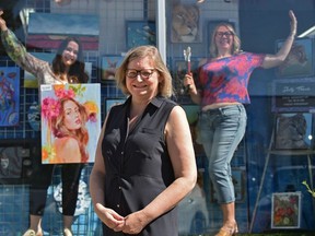 Whyte Avenue Art Walk producer Kim Fjordbotten poses outside as artists Shelly Banks (right) and Oksana Zhelisko pose in the window display of The Paint Spot in Old Strathcona.