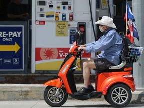 A man wearing a mask drives a mobility scooter along the sidewalk past a gas station on Portage Avenue in Winnipeg on Monday, July 20, 2020.