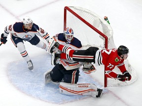 Kirby Dach #77 of the Chicago Blackhawks gets tripped up against Mikko Koskinen #19 and Caleb Jones #82 of the Edmonton Oilers during the second period in Game 3 of the Western Conference Qualification Round at Rogers Place on August 05, 2020.