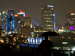 A walker with an umbrella looks out over the city on a rainy night along Saskatchewan Drive in Edmonton, on Tuesday, Aug. 11, 2020.