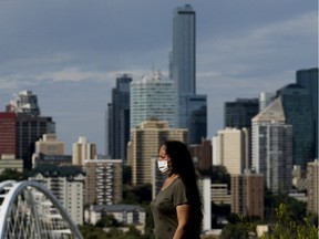 The Edmonton skyline is visible in the background as a woman wearing a face mask walks along Saskatchewan Drive, Aug. 17, 2020. The city of Edmonton was placed on the province's COVID-19 watch list.