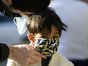 A father helps his young son put on a face mask before entering a shop in Edmonton during the coronavirus pandemic on Friday September 11, 2020.