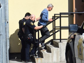 John Brittain is led into the courthouse in Penticton to face three charges of first degree murder and one count of second degree murder.