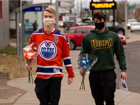 Dawson Hartman, left, and Nathan Makarowski lay flowers and pucks in honour of beloved locker room attendant Joey Moss at the mural by Ian Mulder on 99 Street and 71 Avenue in Edmonton, on Tuesday, Oct. 27, 2020. They are starting a petition at Change.org to place a statue of Joey Moss singing O Canada beside that of his friend Wayne Gretzky outside of Rogers Place.