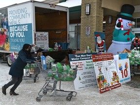 A volunteer pushes a cart full of donations as Can Man Dan, Dan Johnstone, right, begins his 10th year of braving the cold temperatures to raise food and funds to support the mission of Edmonton's Food Bank at the Belmont Sobeys on Thursday, Nov. 19, 2020.