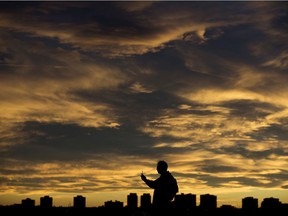 A man takes pictures of the late afternoon clouds near Jasper Avenue and 96 Street, in Edmonton Monday Nov. 2, 2020.