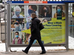 A woman in a mask passes an City of Edmtonon bus stop sign speaking to wearing masks during the COVID-19 pandemic near 111 Street and 82 Avenue in Edmonton, on Monday, Dec. 21, 2020.